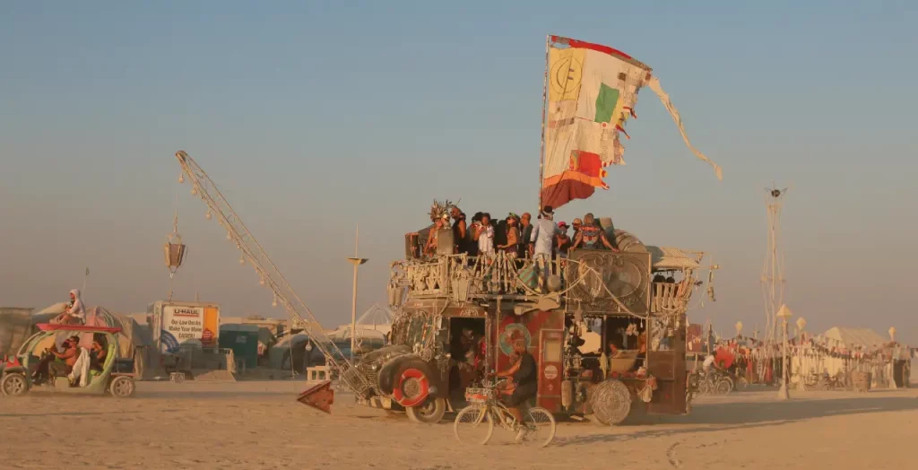 Teilnehmer des Burning Man Festivals in Nevada, USA, feiern auf einem kunstvoll dekorierten Fahrzeug. [Bildquelle: © Following NYC | Canva]