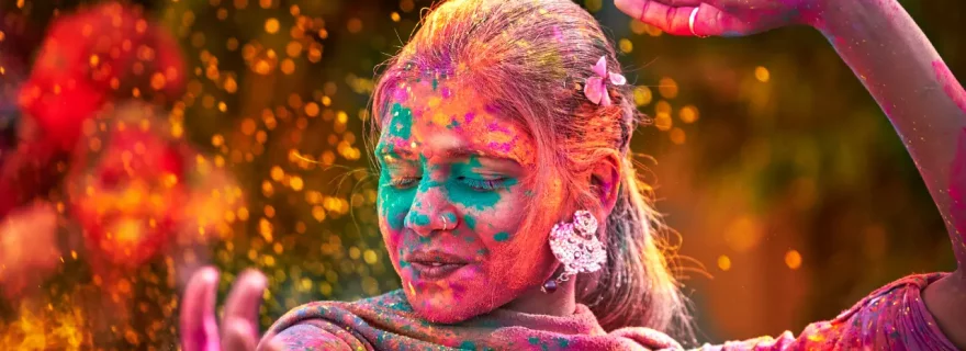 Frau beim Holi Festival in Indien, die mit buntem Pulver bedeckt ist und freudig tanzt.