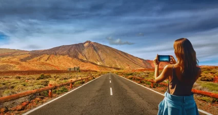 Frau fotografiert eine Straße mit Blick auf den Teide, Teneriffa, Spanien. Vulkanlandschaft und blauer Himmel. [Bildquelle: © csh3d | Canva]