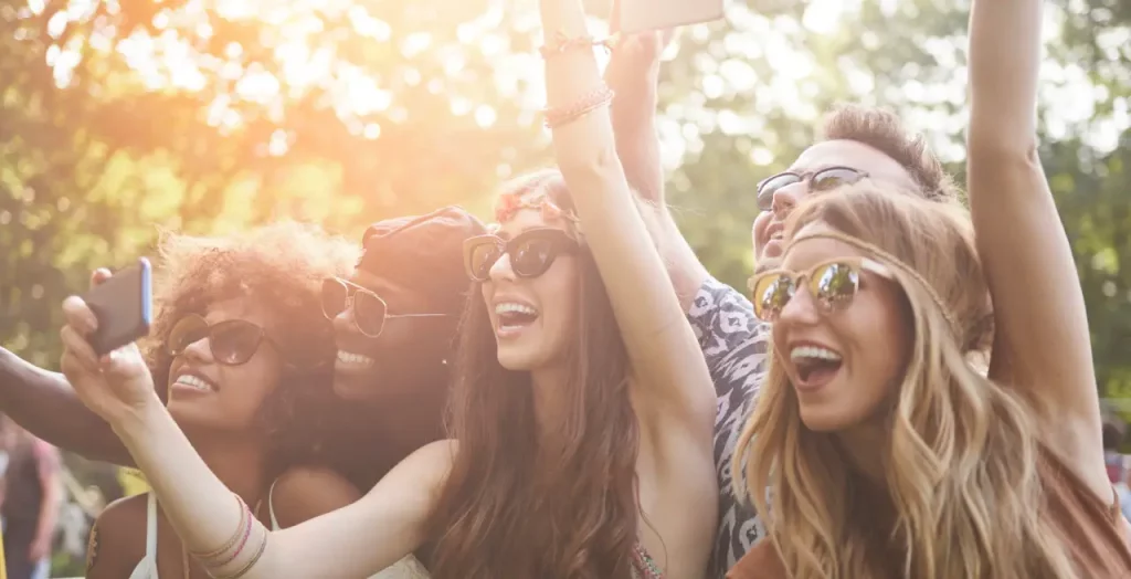 Freunde beim Coachella Festival in Kalifornien, USA, die lachend Selfies machen und Sonnenbrillen tragen.
