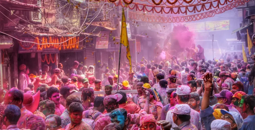Menschenmenge beim Holi Festival in Indien, bedeckt mit buntem Pulver, das in der Luft schwebt. 
[Bildquelle: © Dibakar Roy | Canva]
