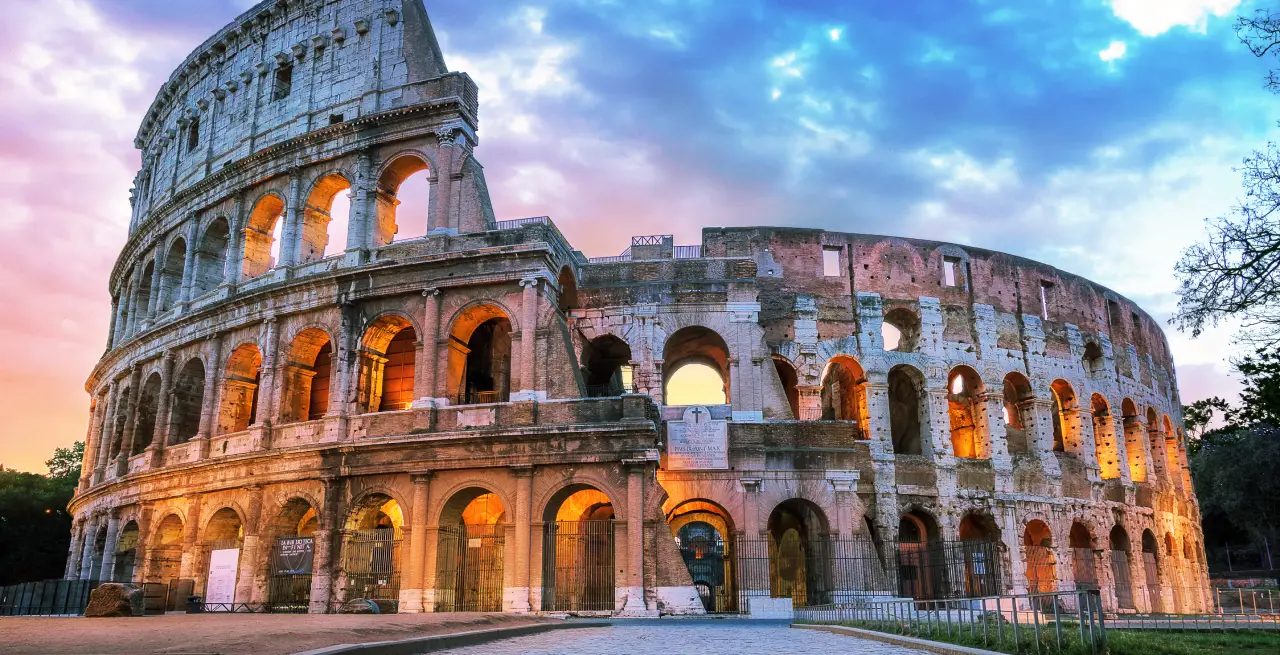 Das Kolosseum in Rom bei Sonnenuntergang mit beleuchteten Bögen und dramatischem Himmel in Italien